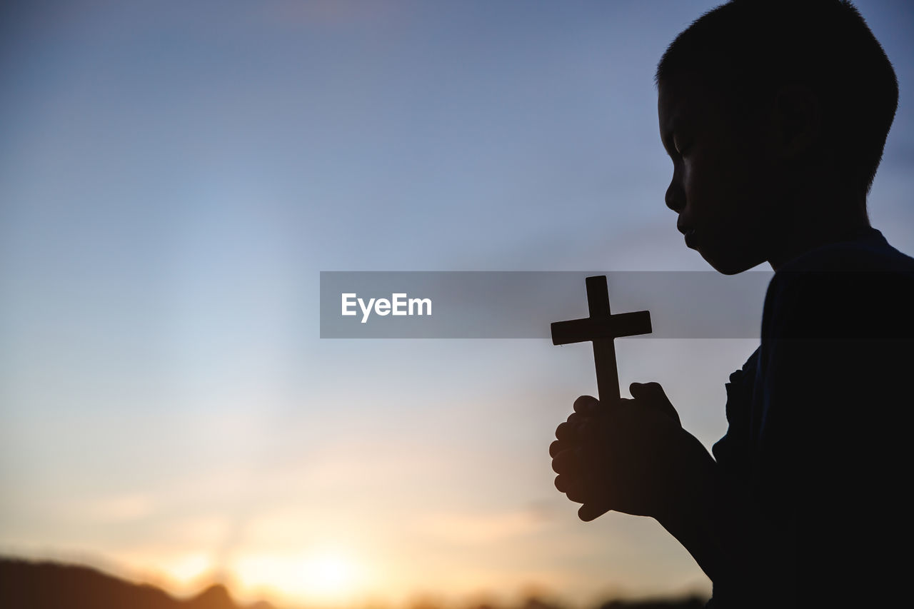 SILHOUETTE BOY HOLDING CROSS AT SUNSET