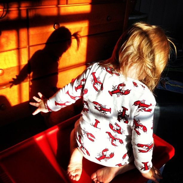 Rear view of a girl sitting with shadow on wall