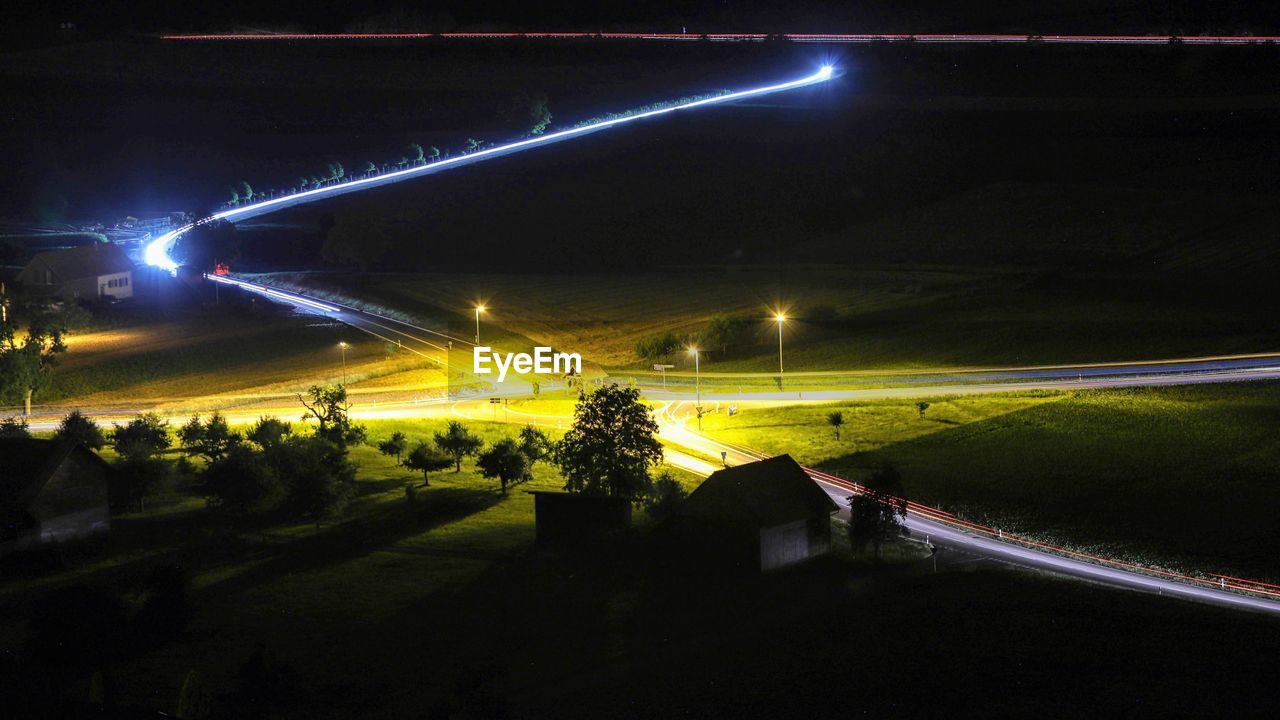 VEHICLES ON ROAD AGAINST ILLUMINATED CITY AT NIGHT