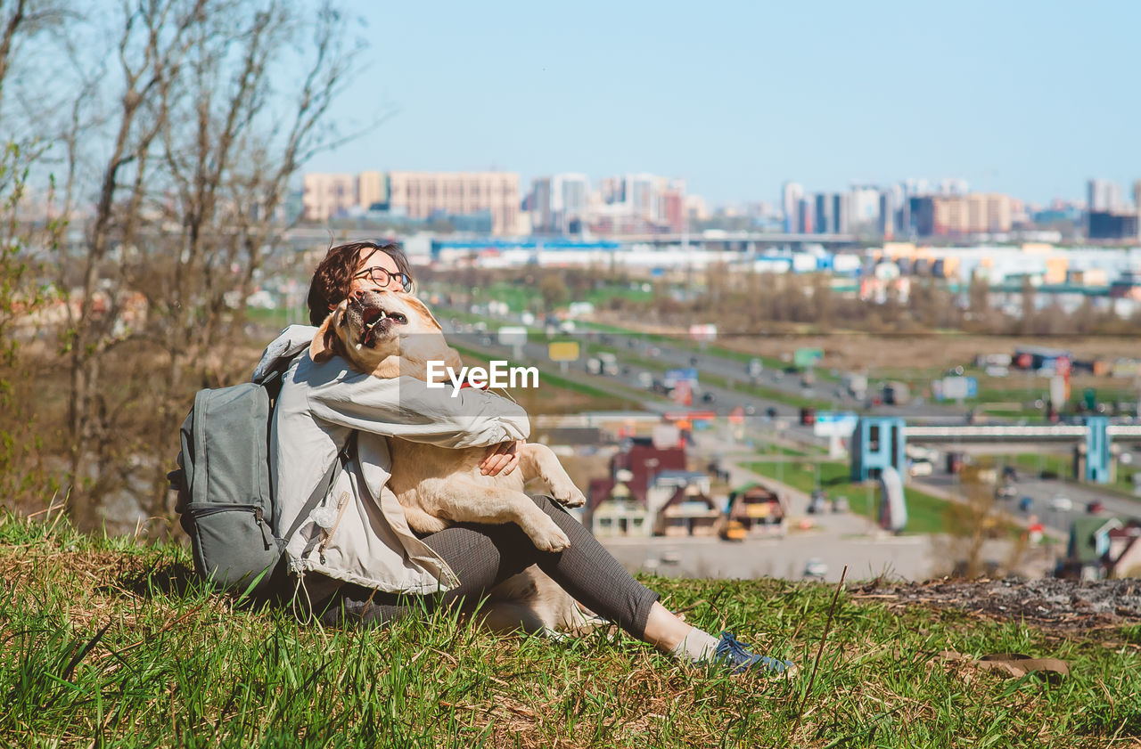 The girl hugs the labrador retriever and laughs, sitting on the mountain. vacation with a dog 