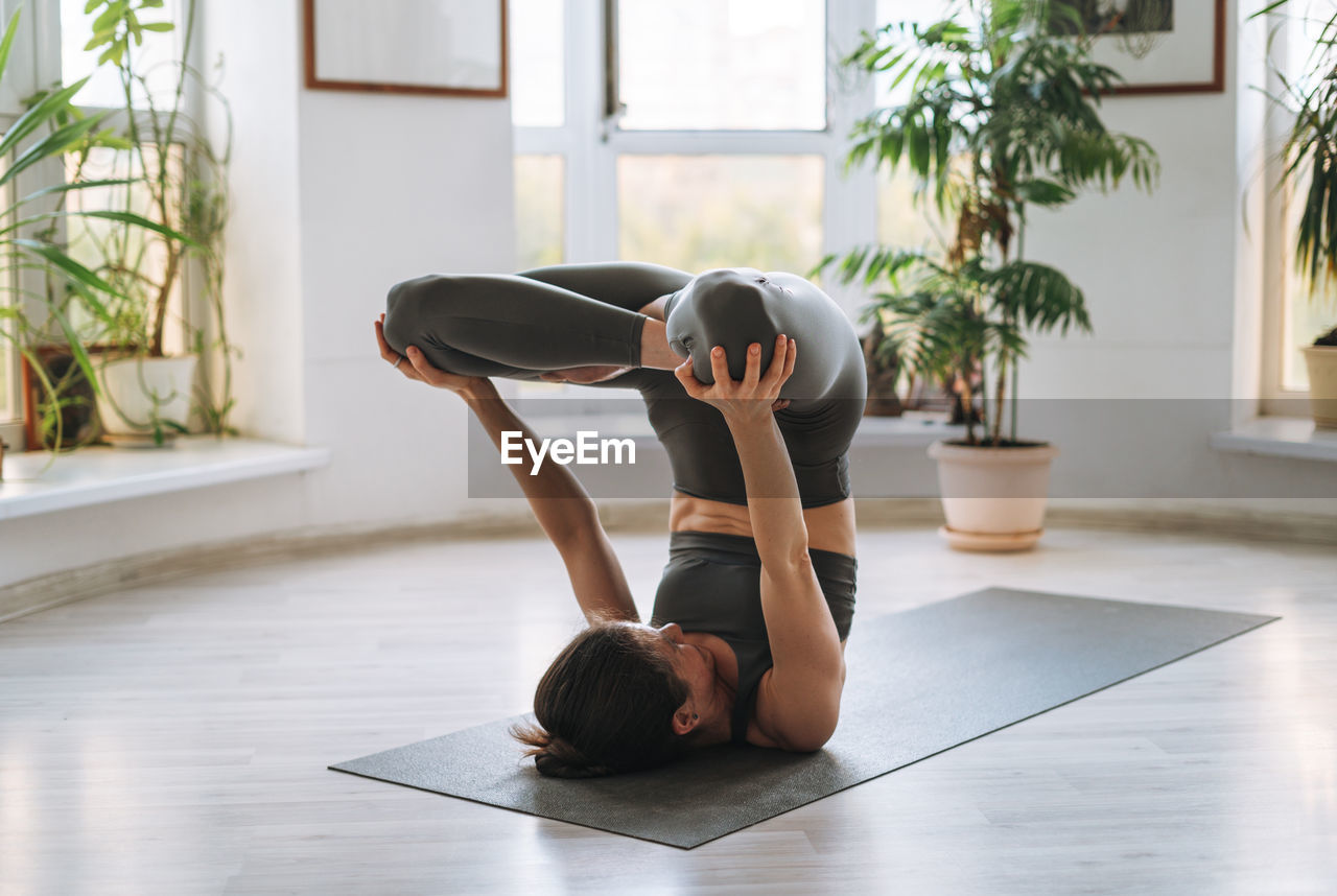 Young fit woman practice yoga doing asana in light yoga studio with green house plant