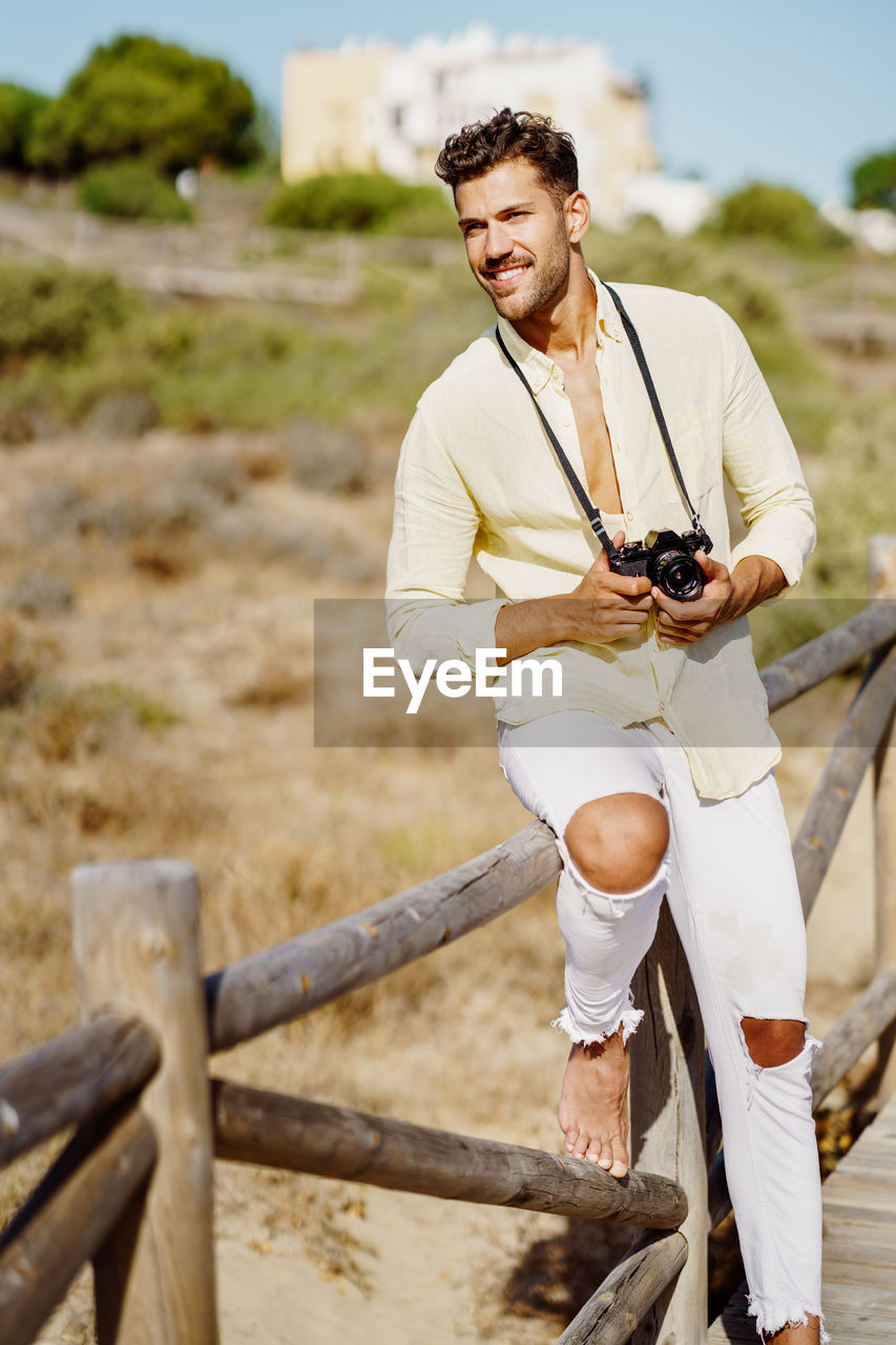 Young man holding camera while standing on land