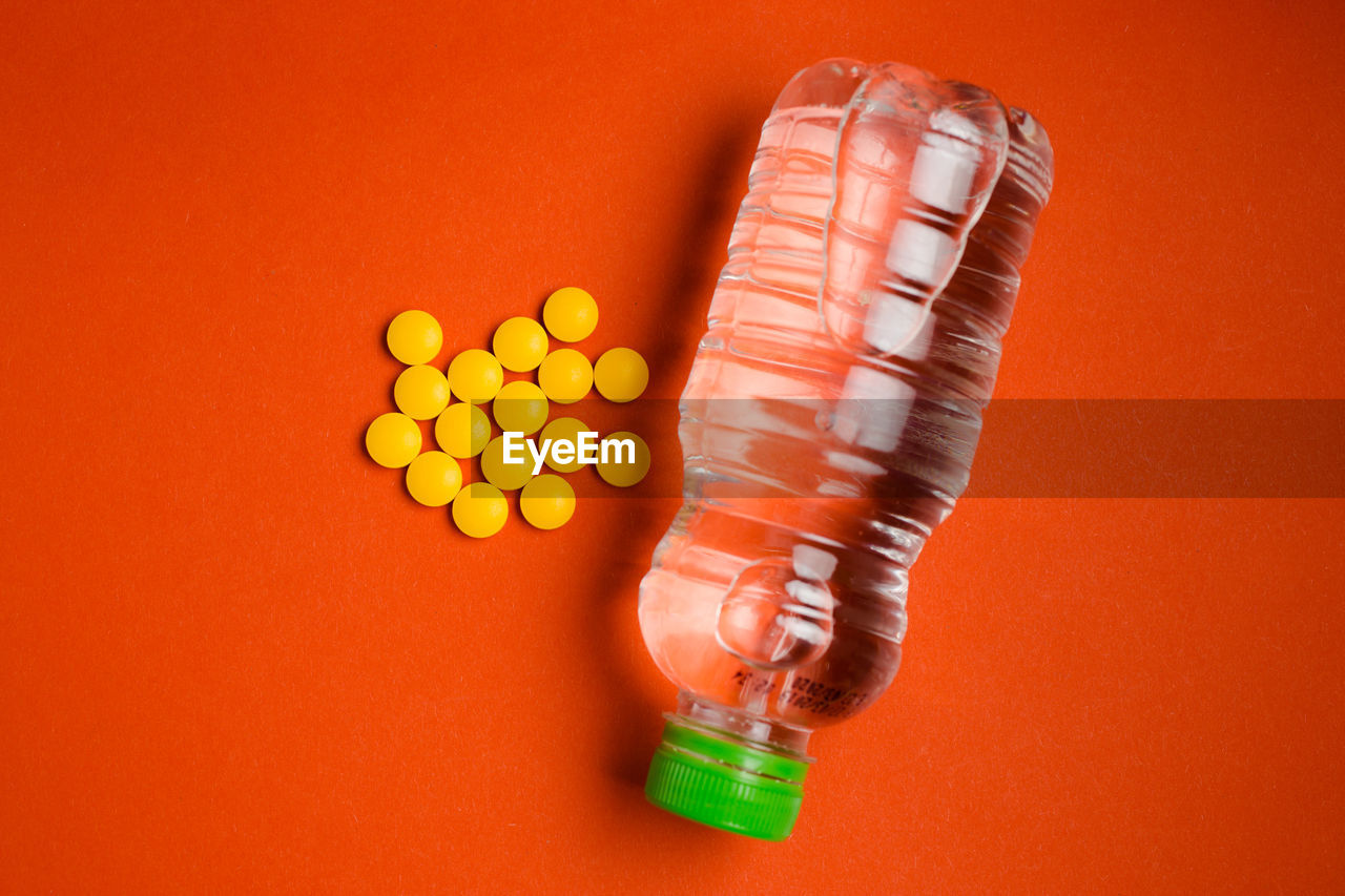 Directly above shot of pills by water bottle against orange background