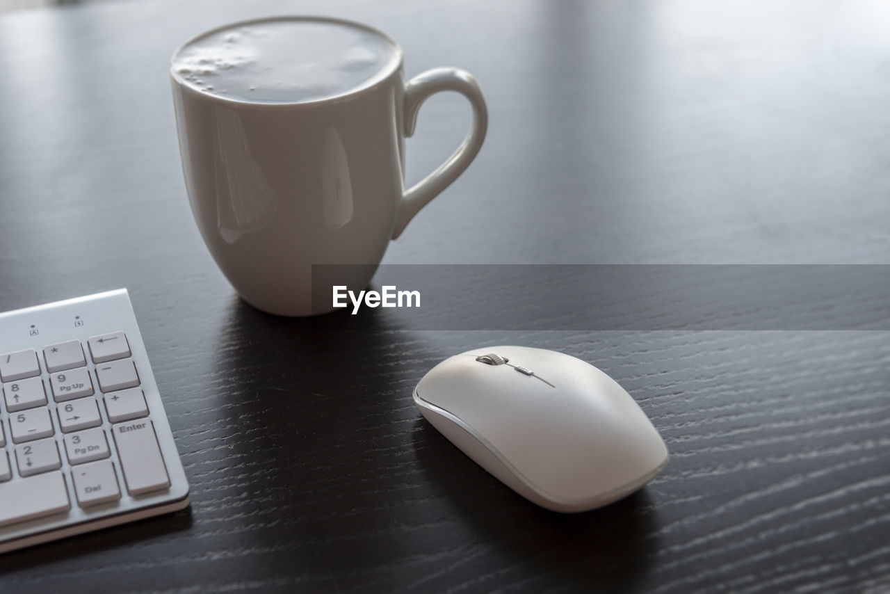 Close-up of coffee cup by keyboard and mouse on table