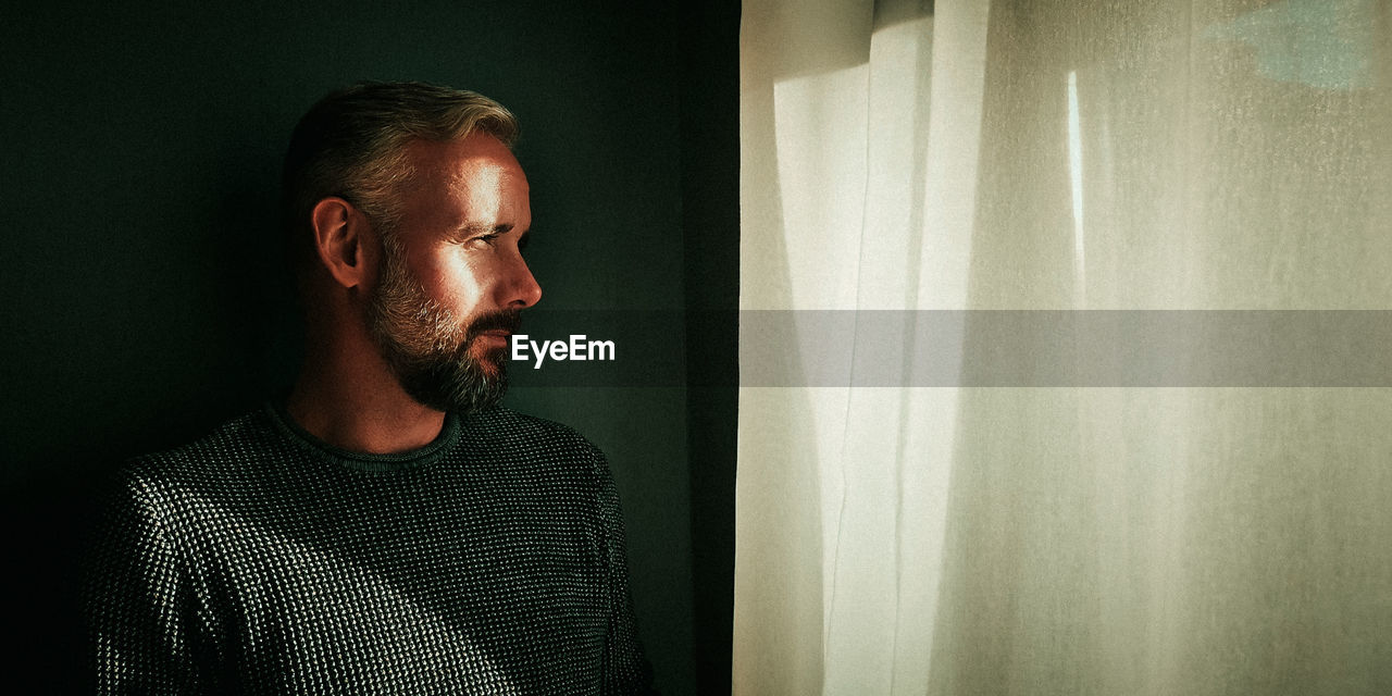 Mature man looking through window at home