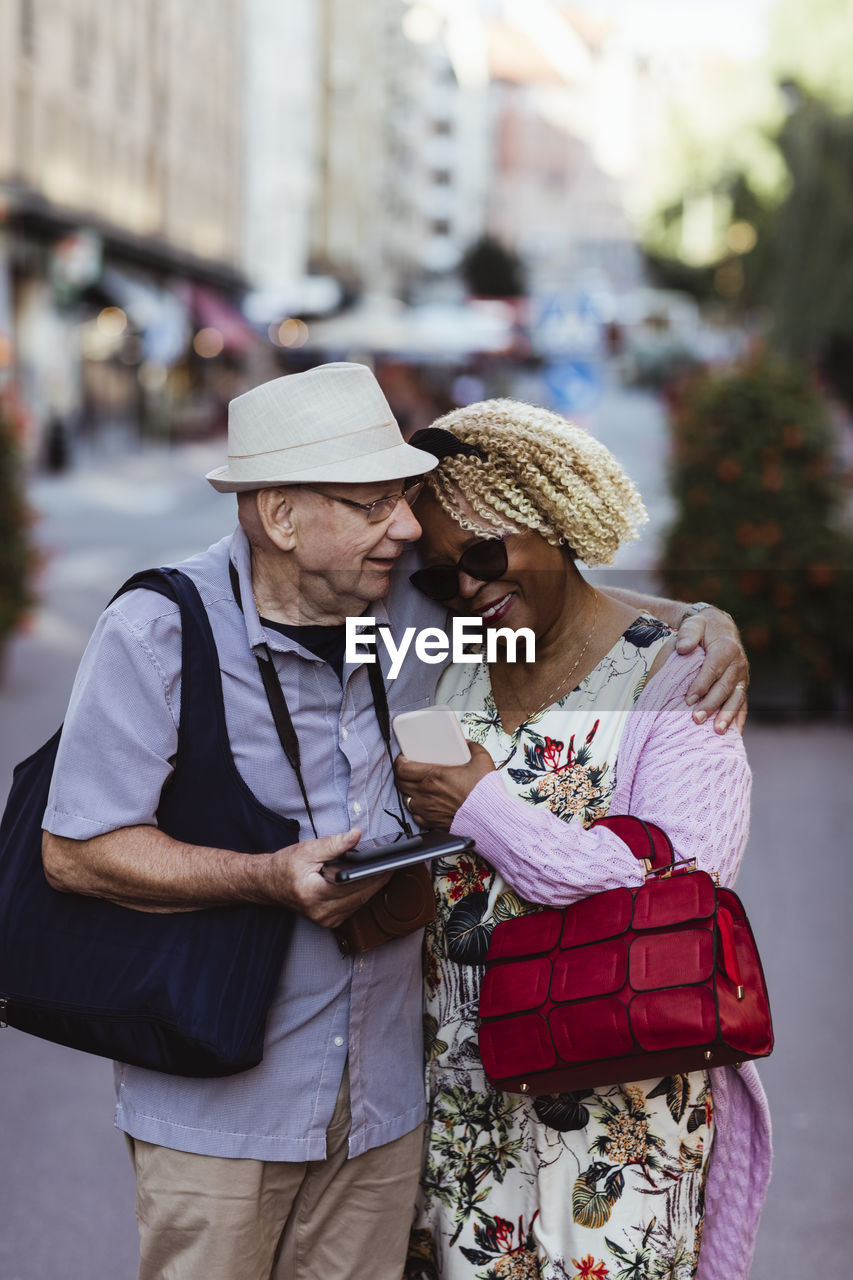 Senior man embracing woman while standing on street in city