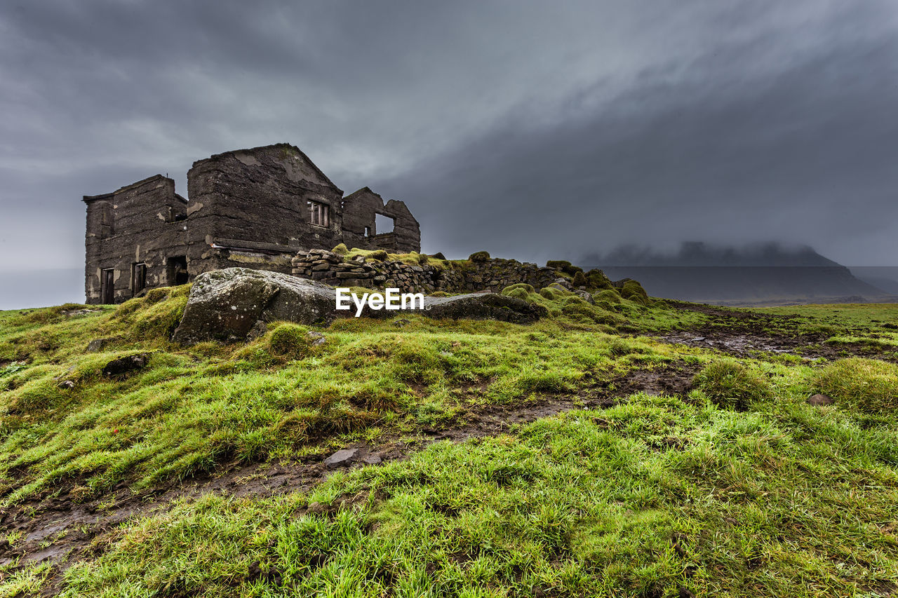 sky, cloud, architecture, hill, history, nature, the past, built structure, rock, environment, land, travel destinations, landscape, building, plant, overcast, old ruin, scenics - nature, travel, building exterior, highland, grass, storm, rural area, no people, tourism, ruins, coast, beauty in nature, ancient, dramatic sky, storm cloud, outdoors, terrain, green, fog, cliff, castle, old, non-urban scene, ruined, sea, cloudscape, plateau, religion, tranquility, atmospheric mood, abandoned, house