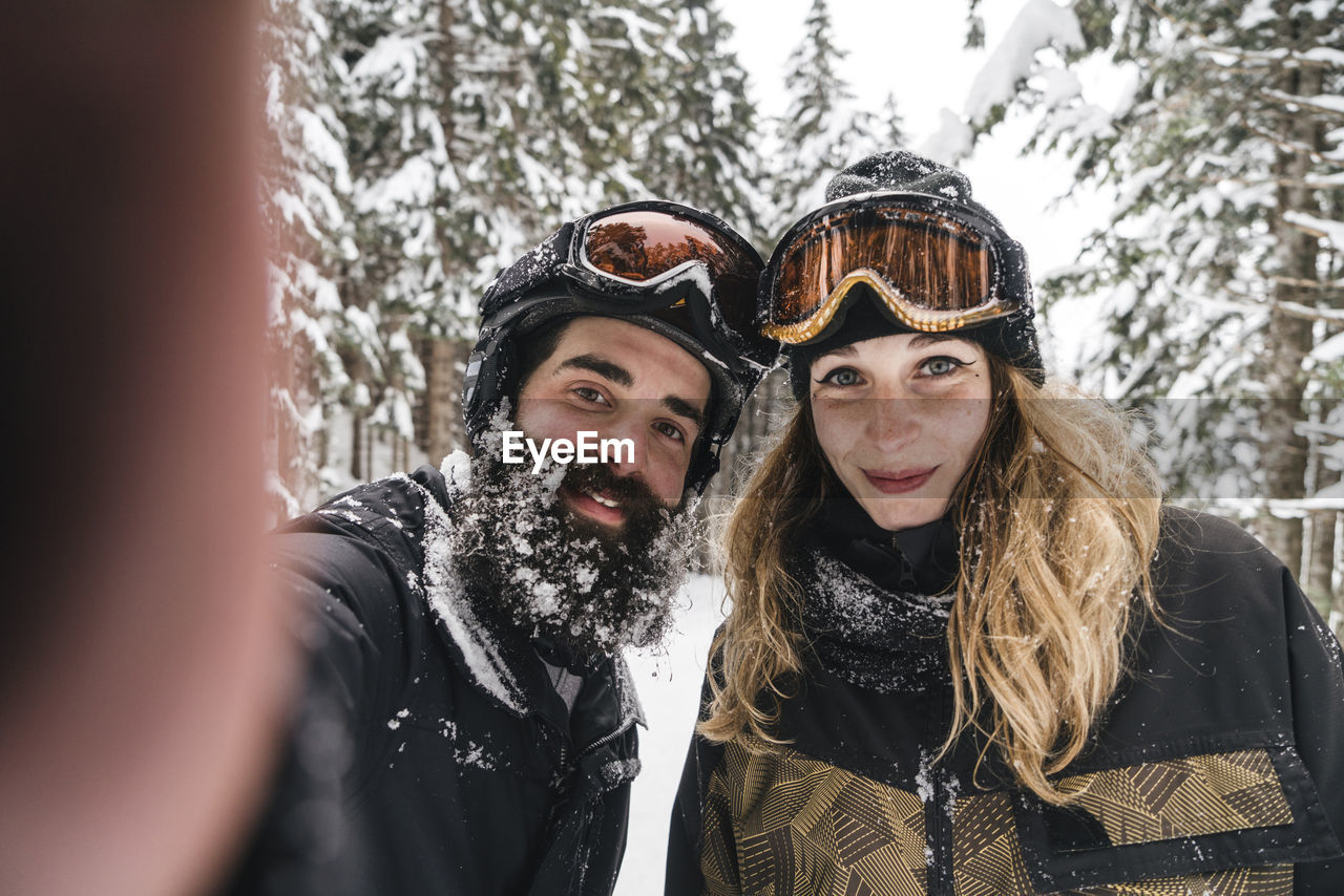 Selfie of smiling couple in skiwear in winter forest