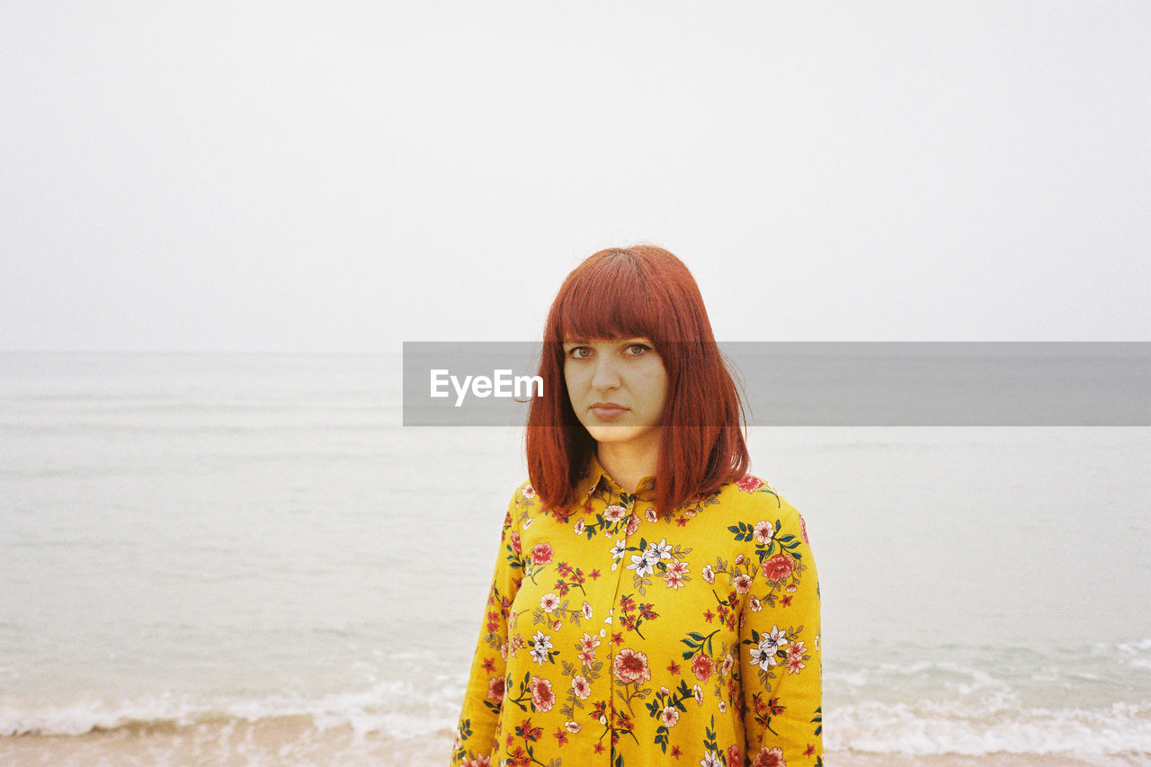 Portrait of beautiful mid adult woman standing at beach against clear sky