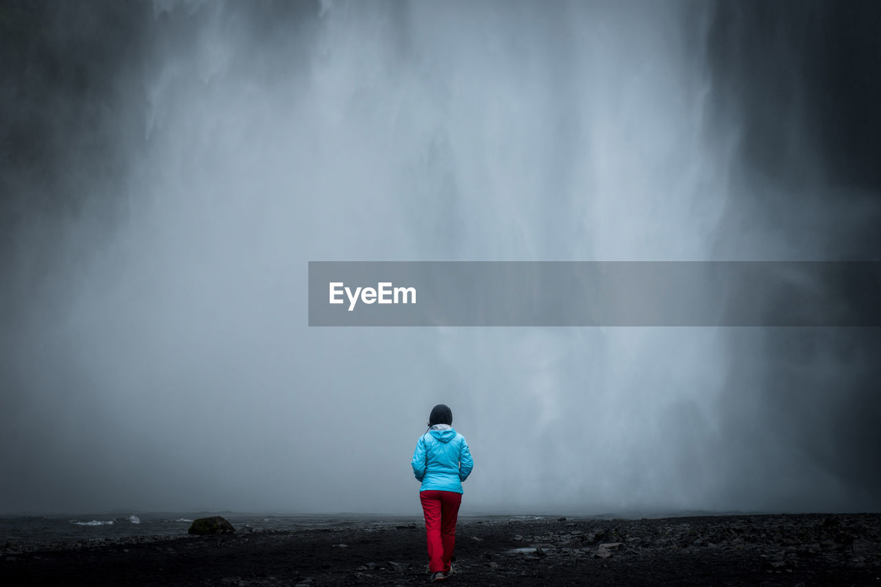 Traveler woman admiring skogafoss waterfall, in southern iceland