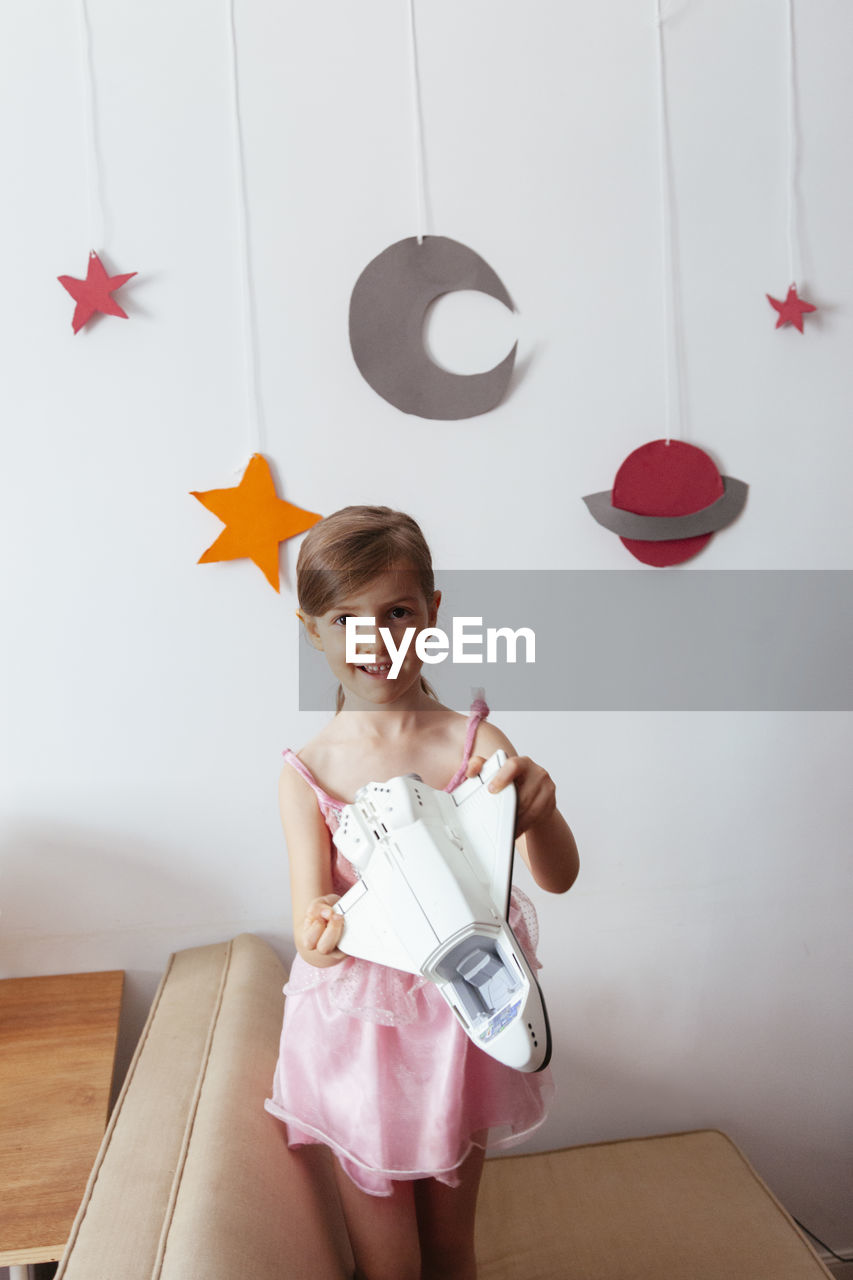 Portrait of smiling girl holding toy against wall at home