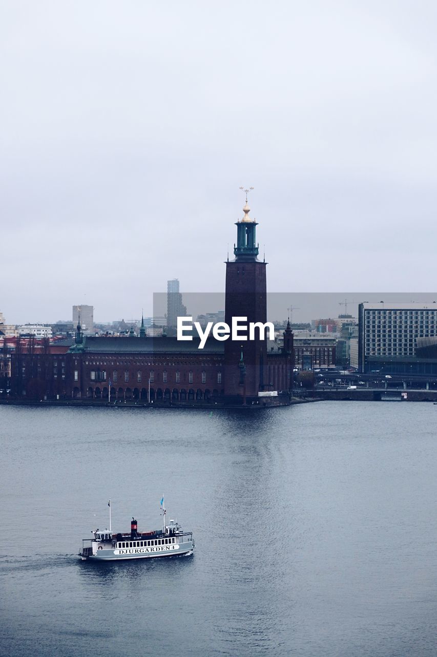 BOAT SAILING ON RIVER BY BUILDINGS AGAINST SKY