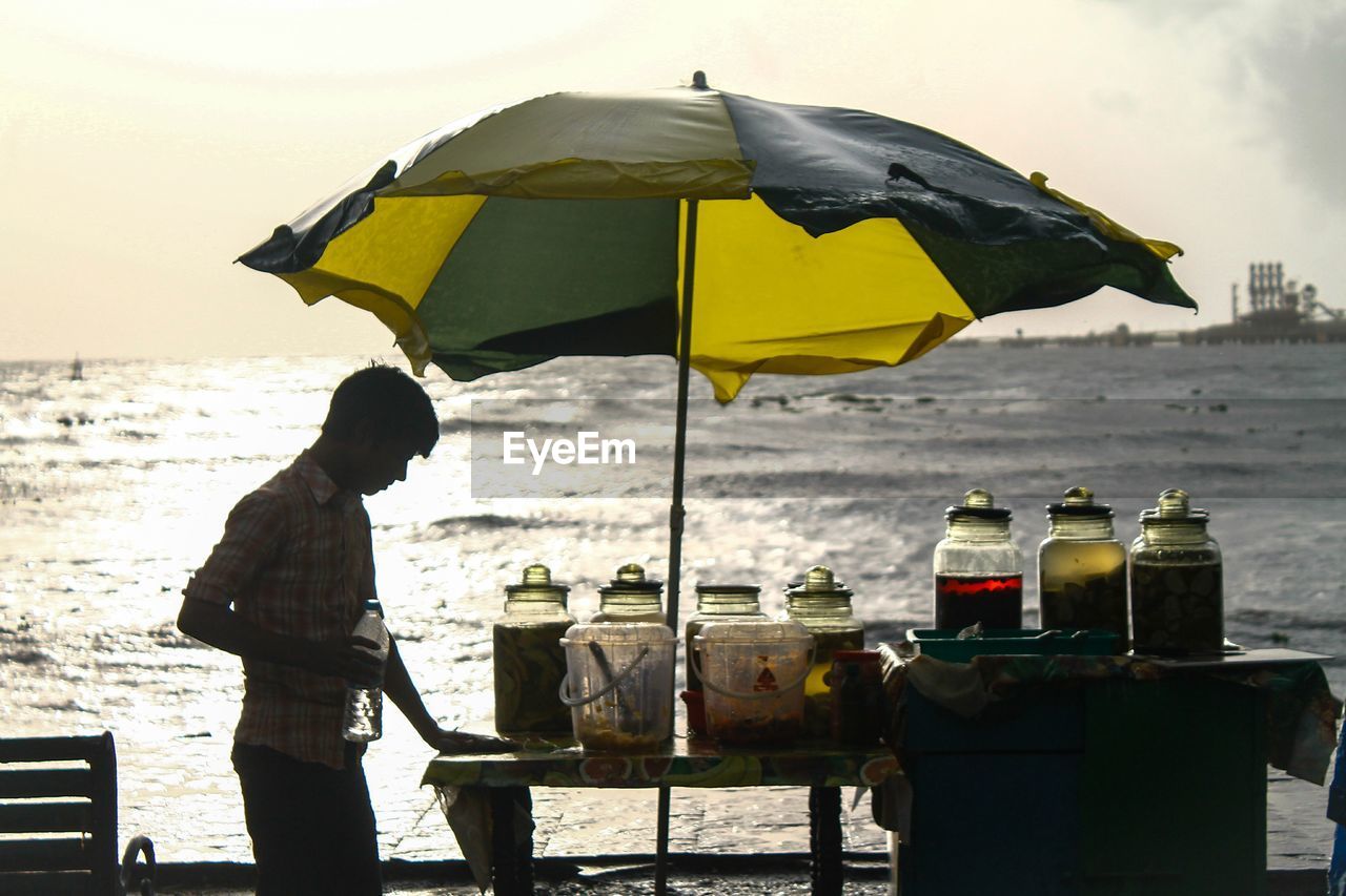 Man cleaning table at beach against sky