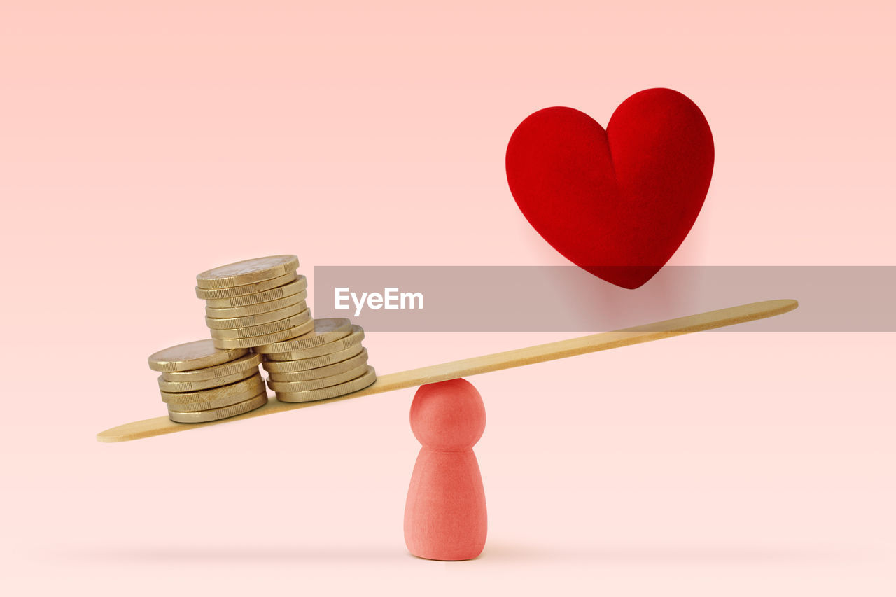 Money and heart on scale on pink background- concept of woman and money priority over love in life