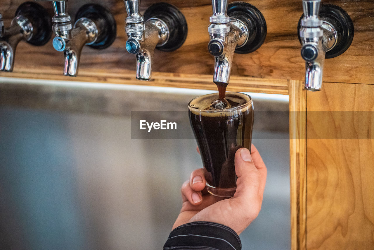 Close-up of hand pouring dark beer tasting from tap