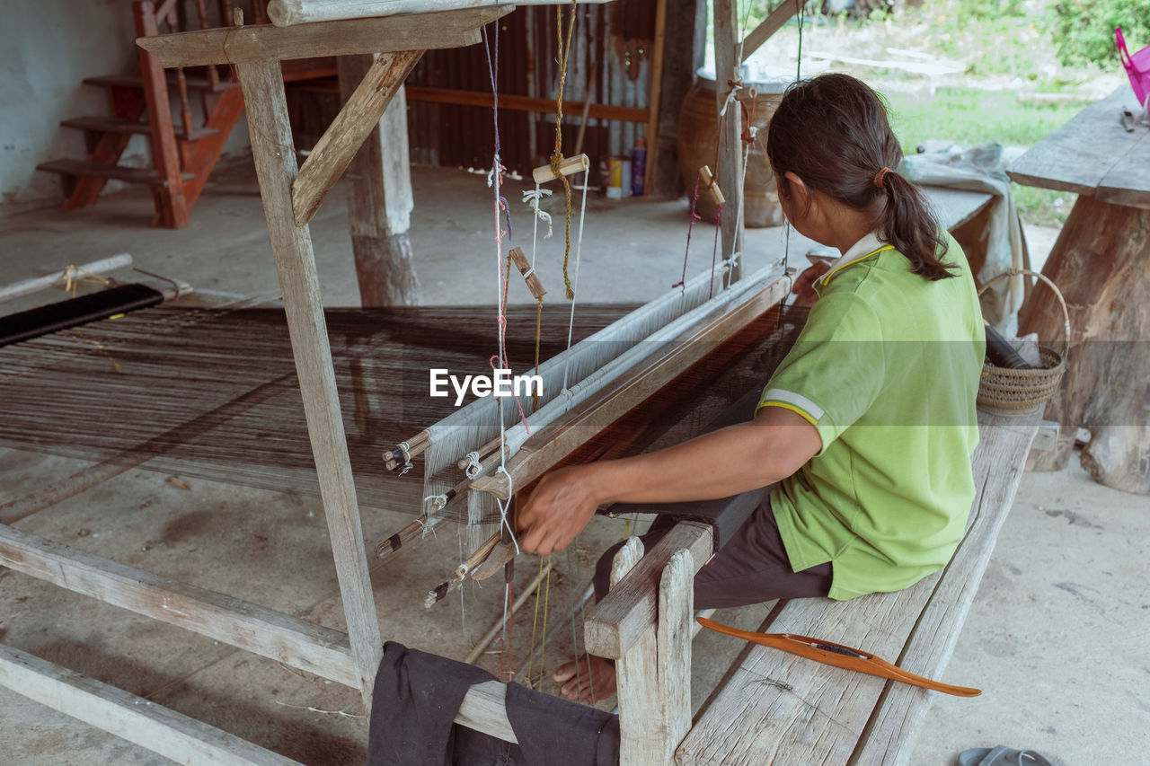 Rear view of woman working on handloom at workshop