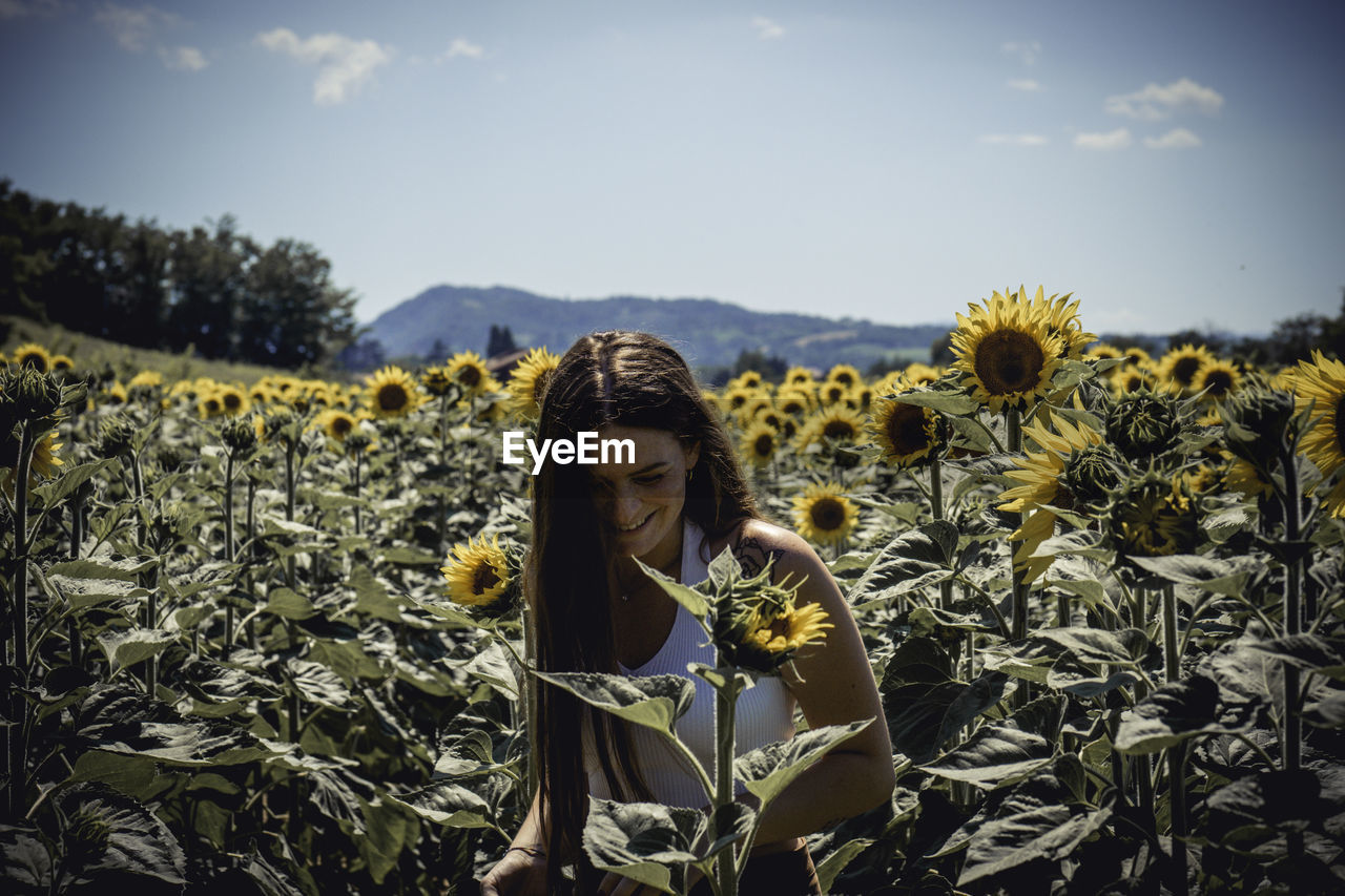 Woman standing at sunflower farm against sky