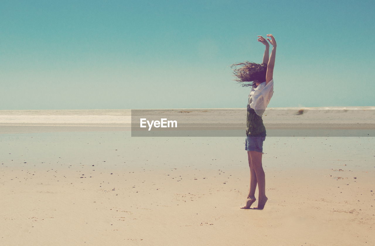 Full length side view of woman standing at beach against sky during sunny day