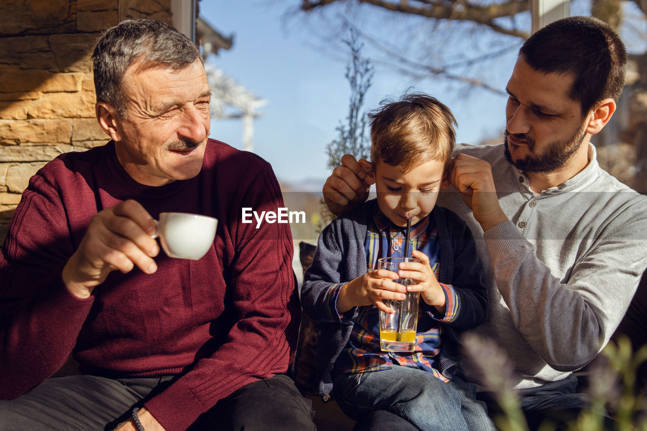 Father looking at son while sitting with grandfather at home