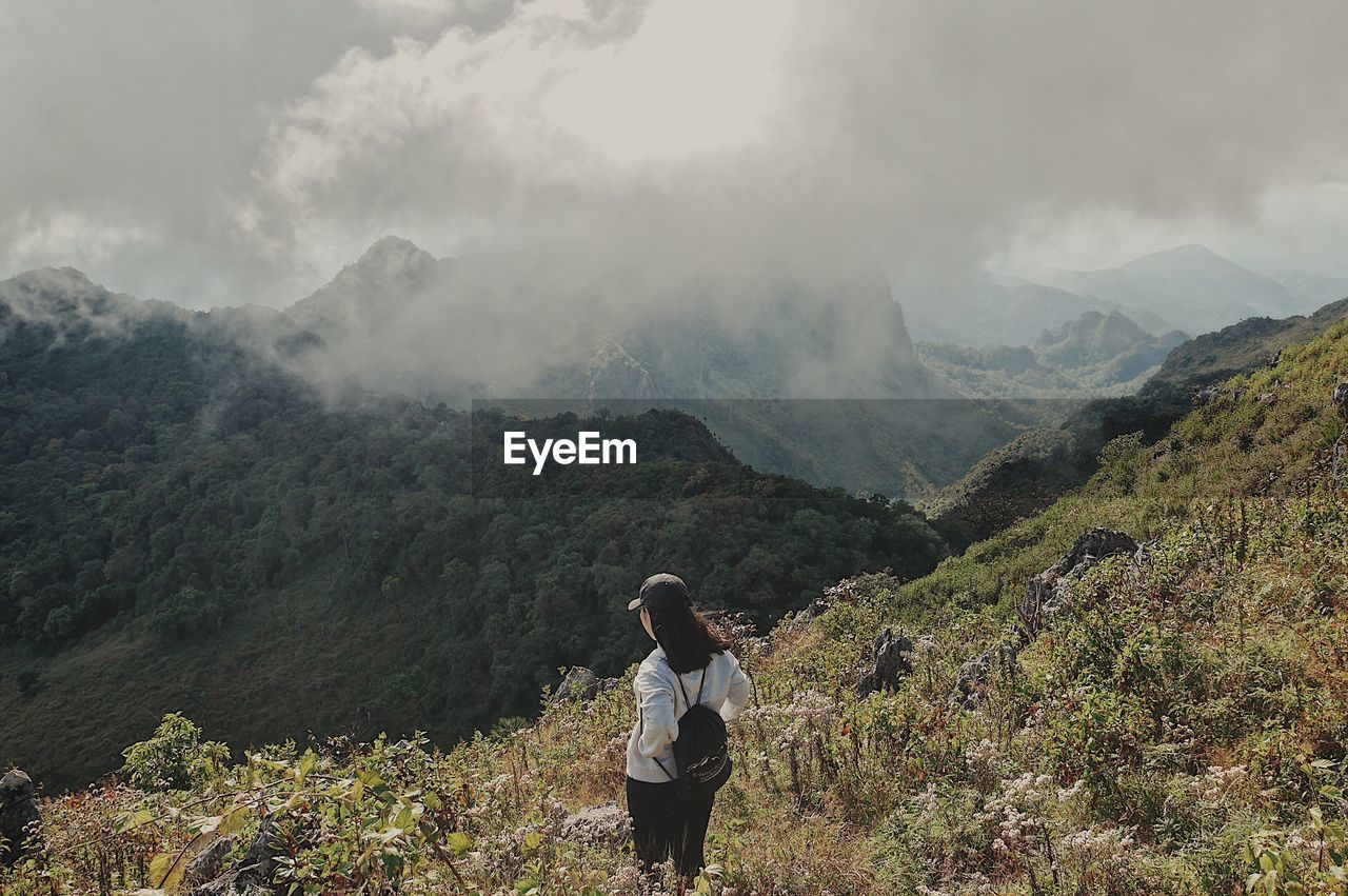 Woman standing on mountain against cloudy sky