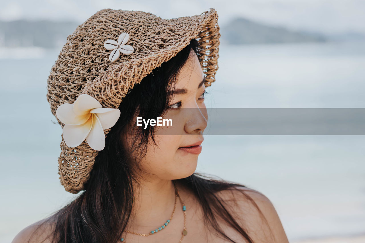 Close-up of woman wearing hat looking away against sea