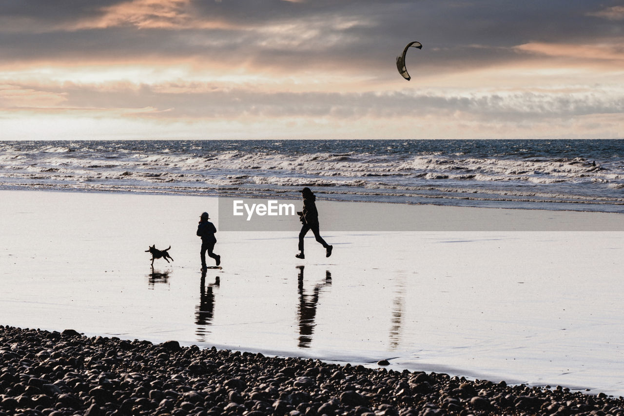 Mother daughter and dog running on the ocean coast at sunset