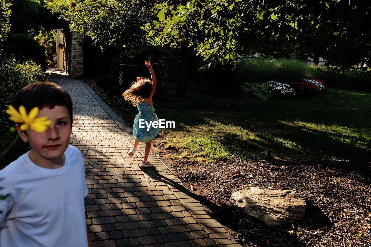 Boy with sister standing on footpath at park