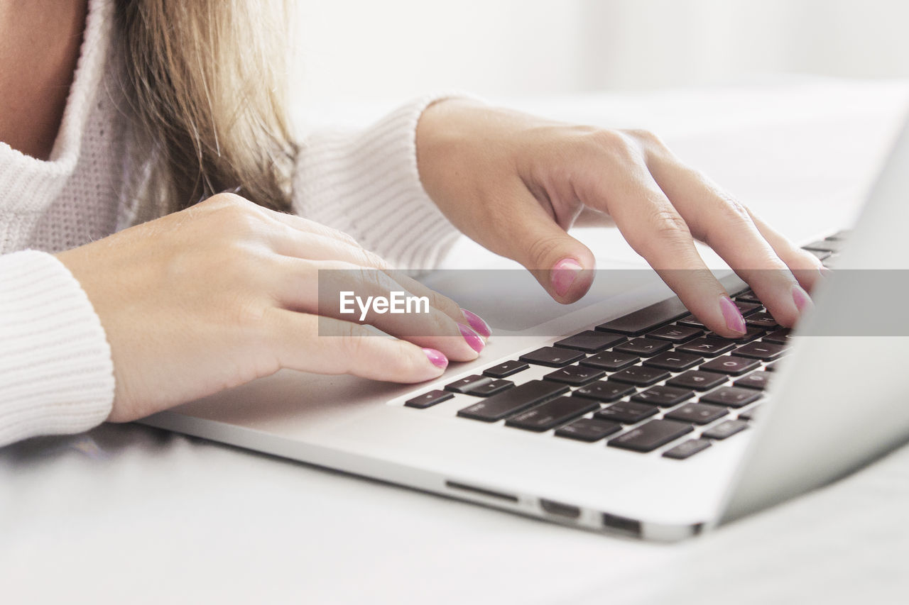 MIDSECTION OF WOMAN USING MOBILE PHONE IN LAPTOP