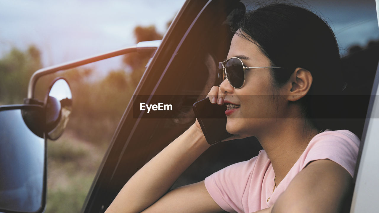 REFLECTION OF WOMAN IN SUNGLASSES SITTING ON CAR