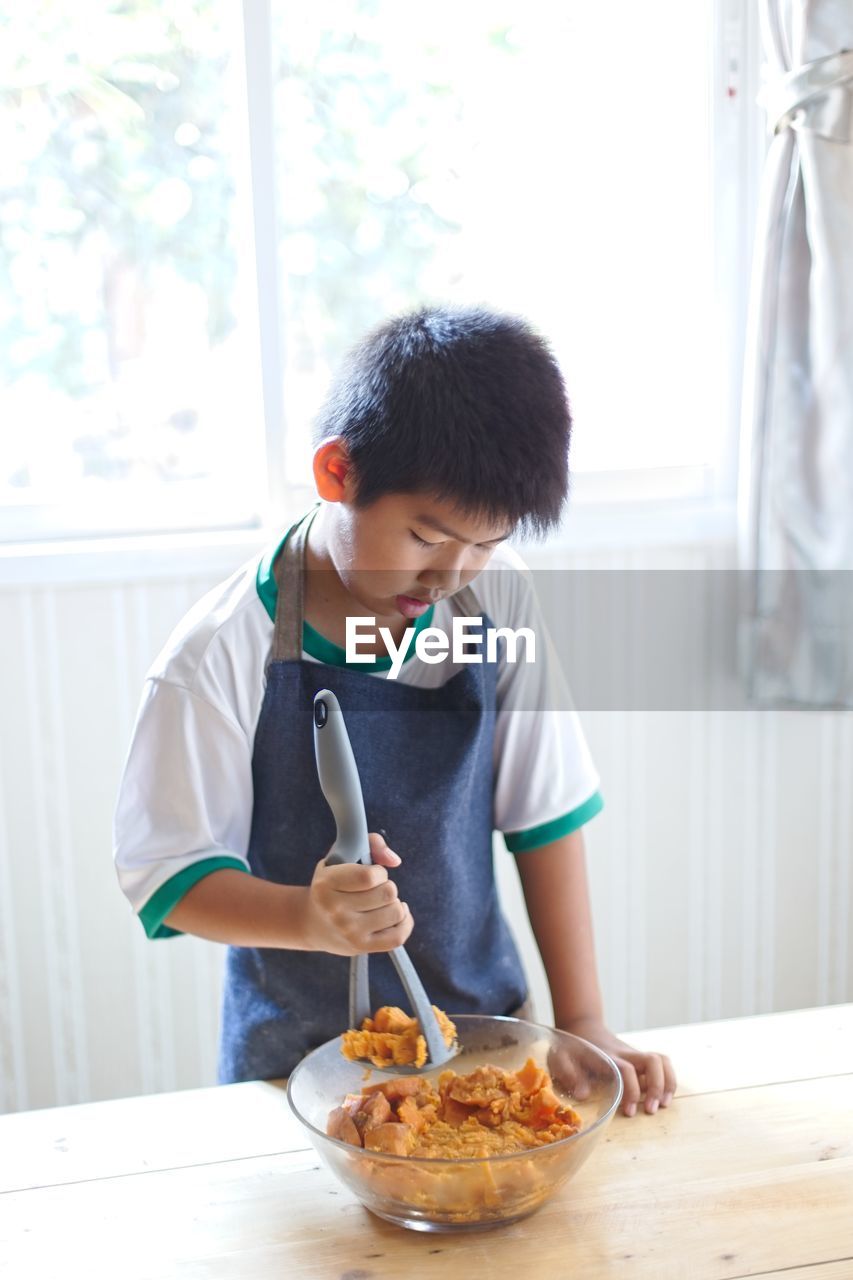 Boy preparing food in bowl on table at kitchen