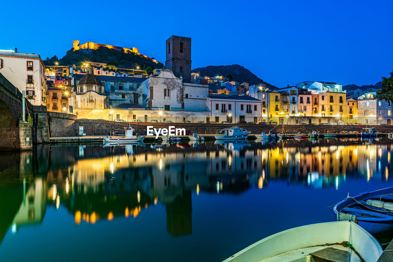 SAILBOATS MOORED ON RIVER BY ILLUMINATED BUILDINGS IN CITY