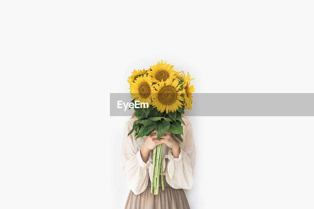 Beautiful young woman in linen dress holding sunflowers bouquet.