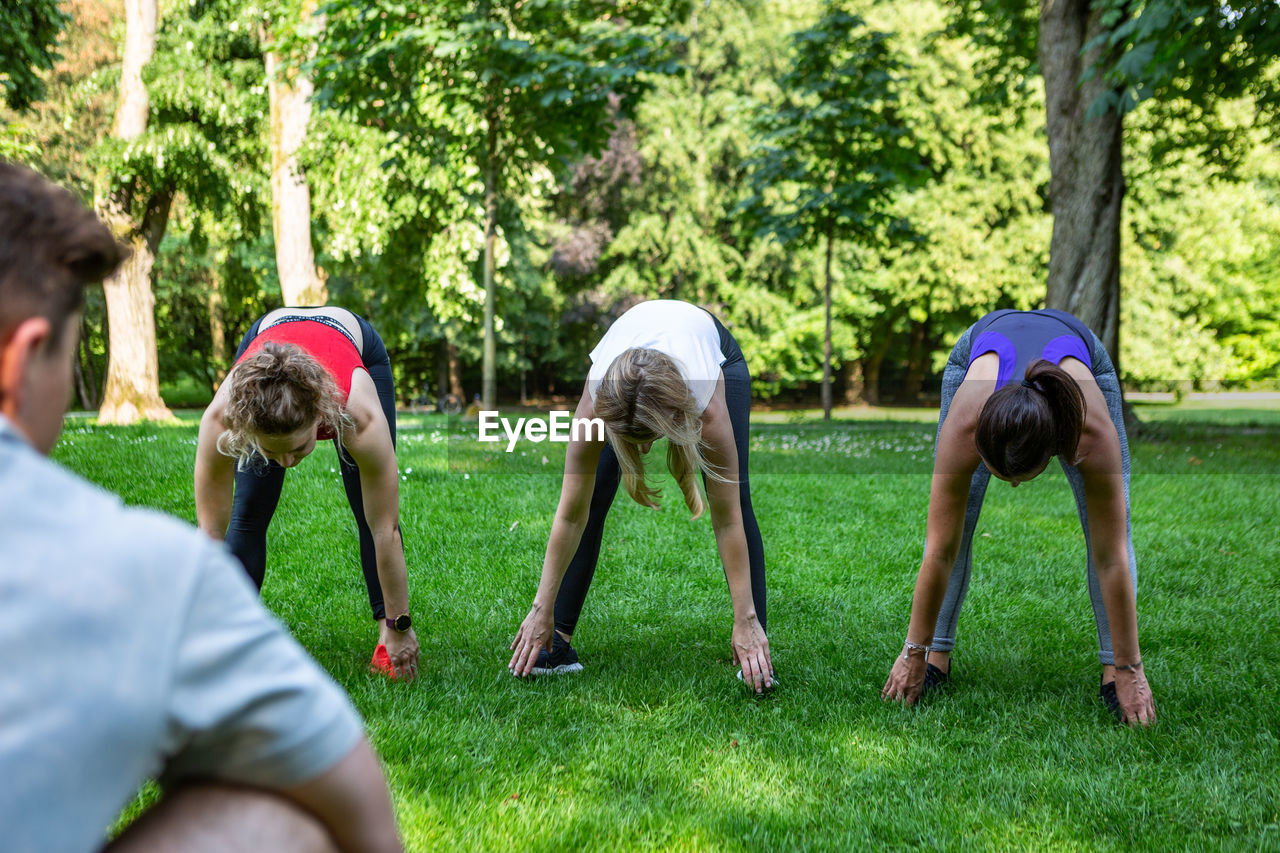 A group of young ladies stretch in front of their male fitness coach in a park in germany