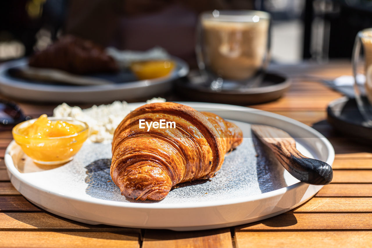 Breakfast with croissant, orange jam and butter with cappuccino in outdoor cafe. sunny morning.