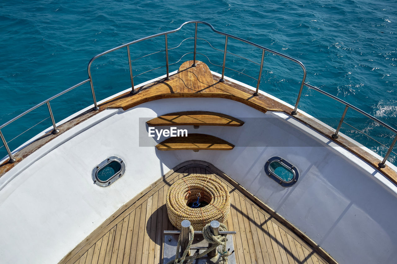 Bow of white yacht on background of blue sea. bay with thick rope lies on wooden deck.