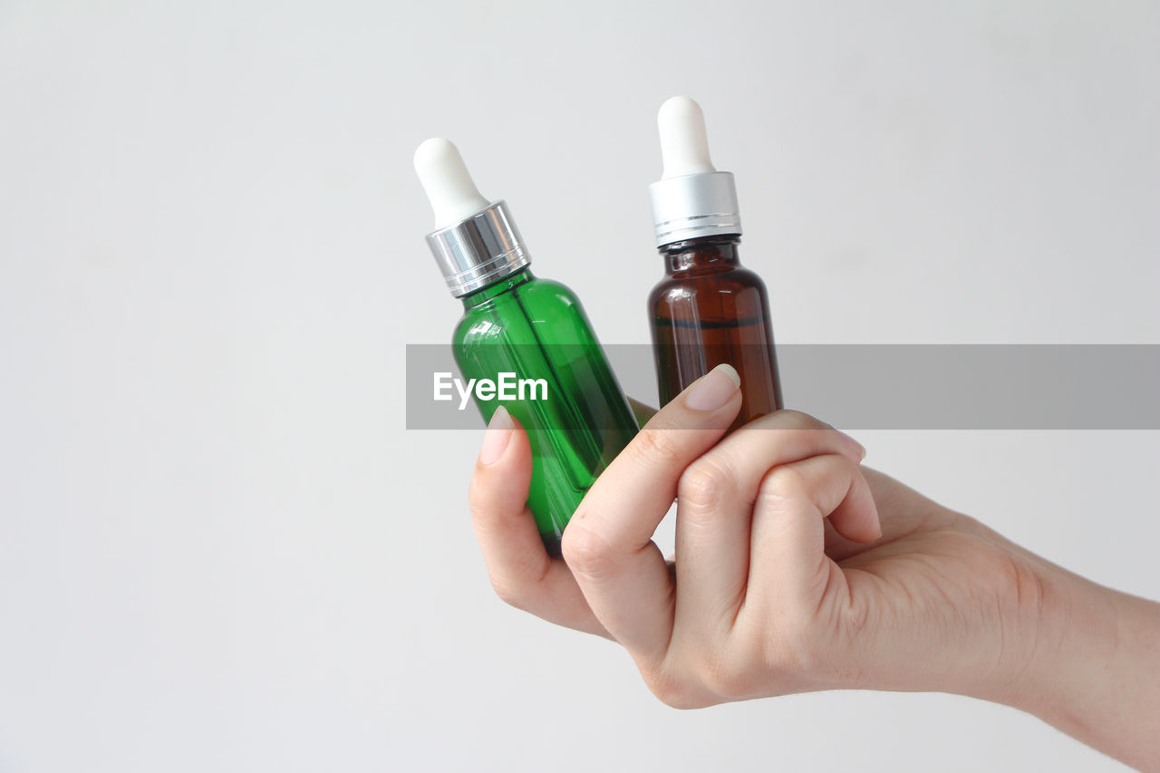 Woman hands holding facial essential oil or serum packaging on white background. 