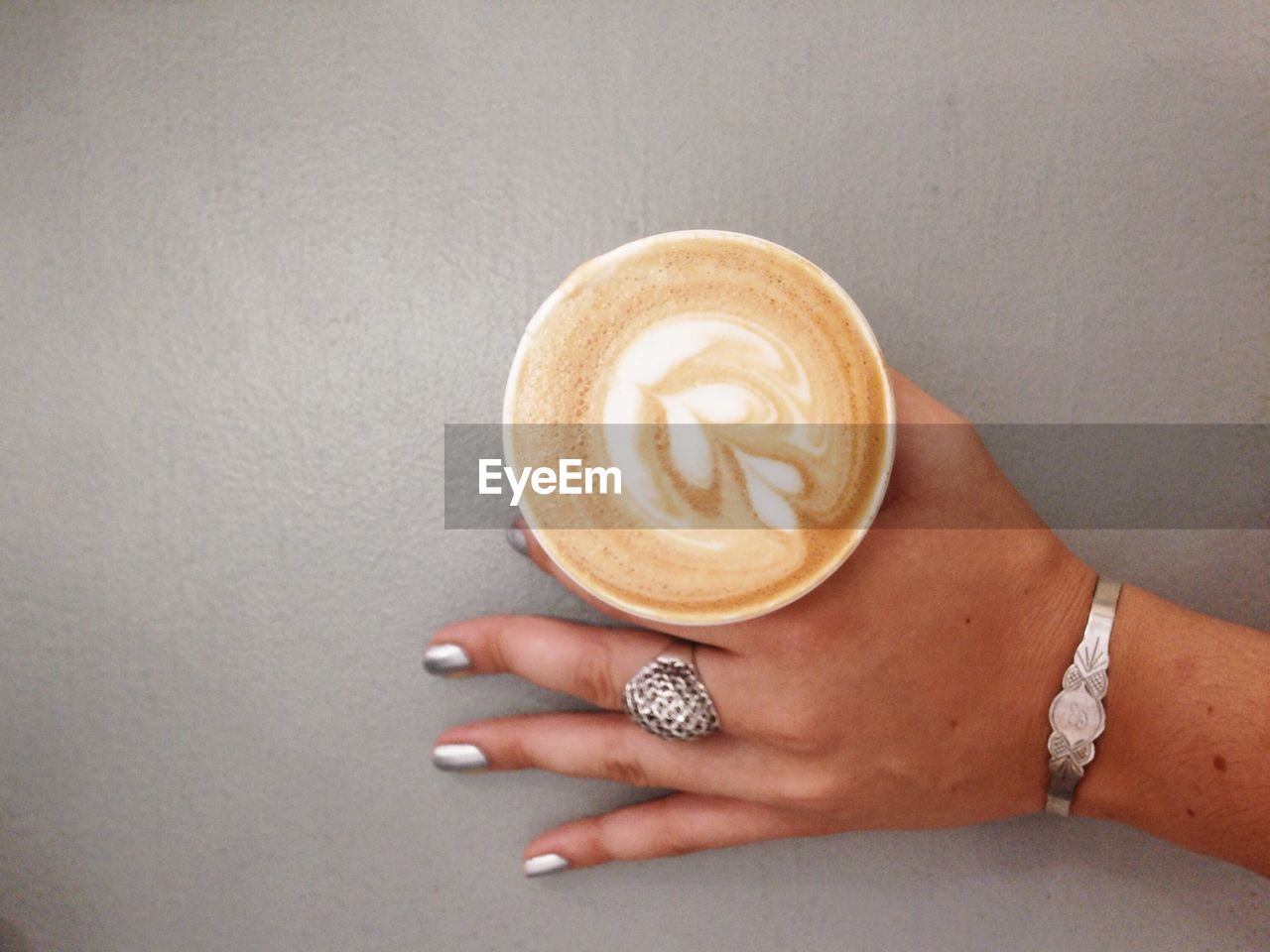 Cropped image of woman holding cappuccino on gray table