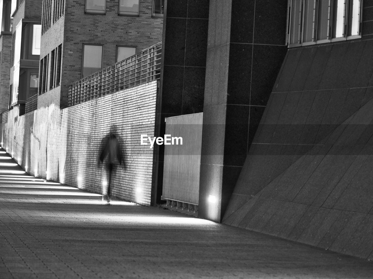 Unrecognizable pedestrian strolling by illuminted walkway at night