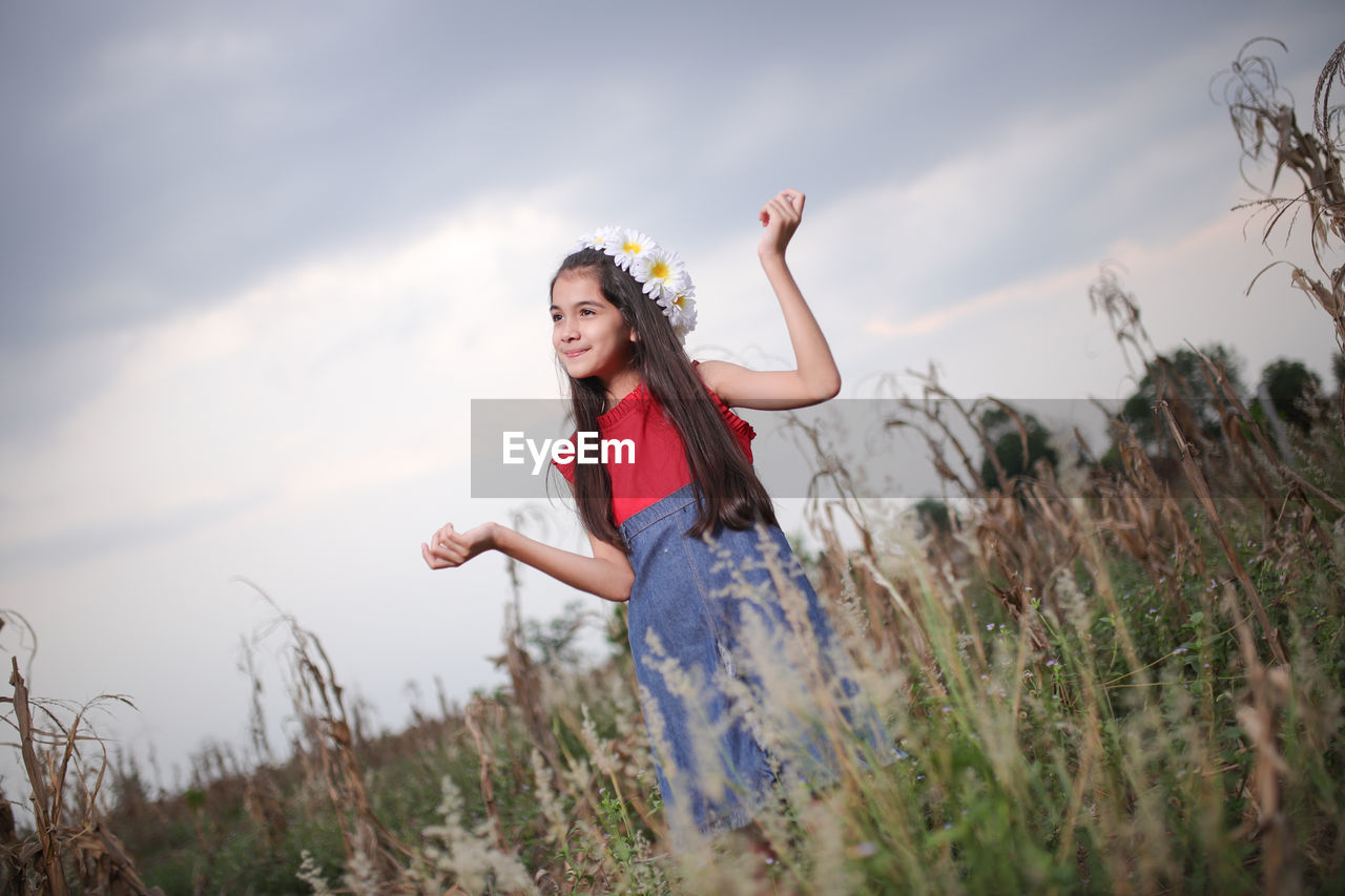 Smiling cute girl standing amidst plants on field during sunset