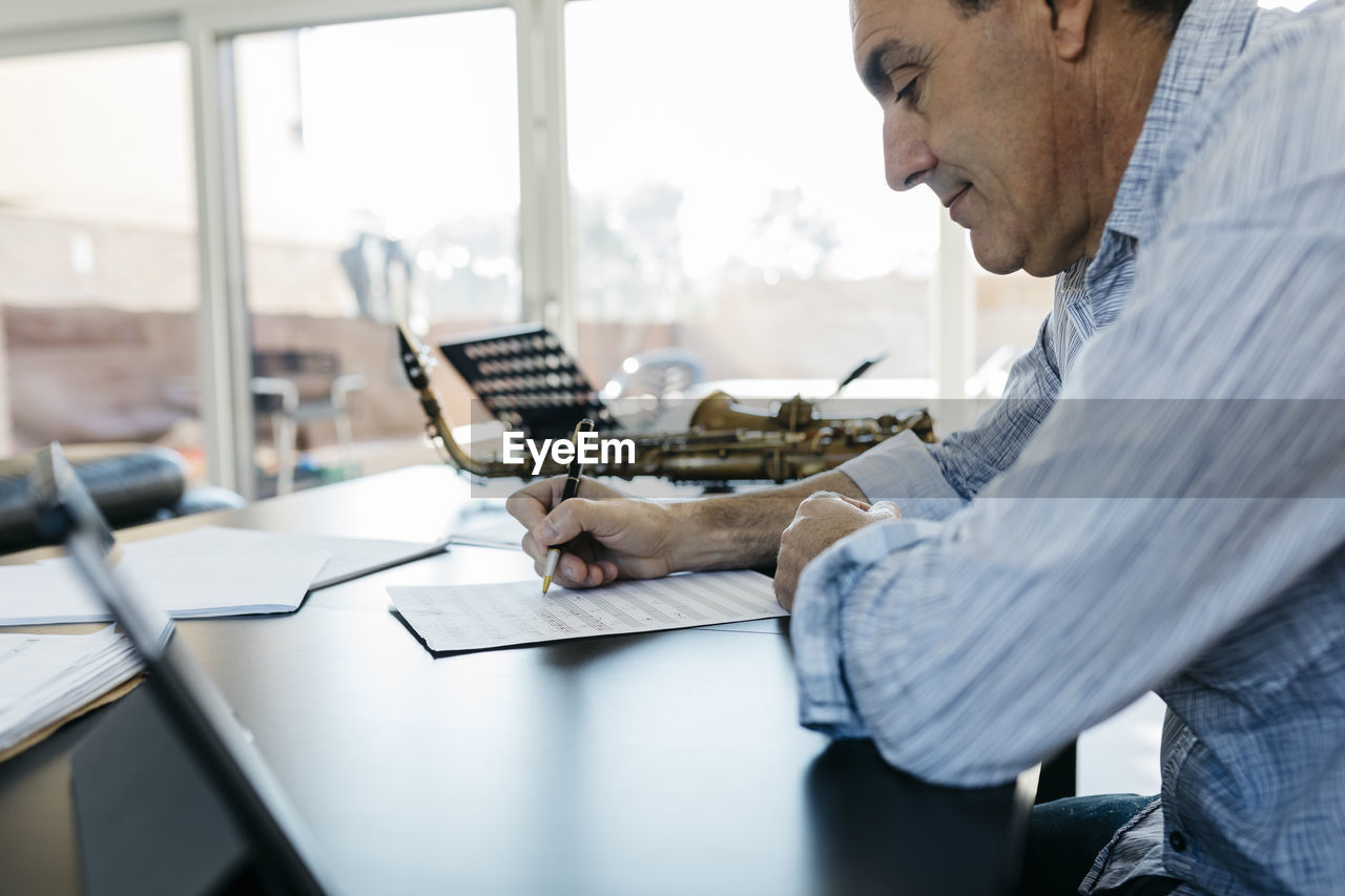 Man writing musical notes on paper sitting at table