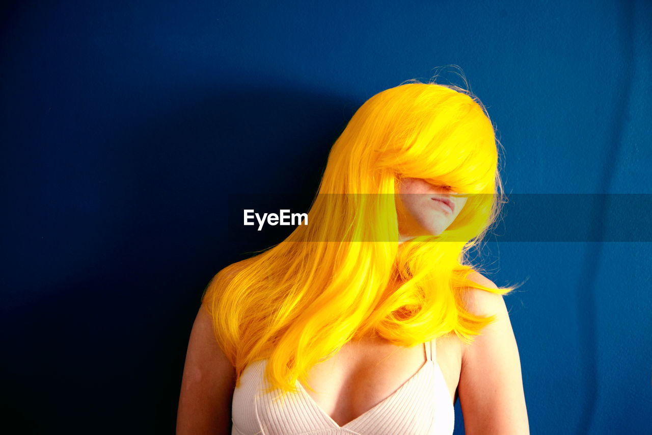 Beautiful young woman wearing yellow wig against blue background