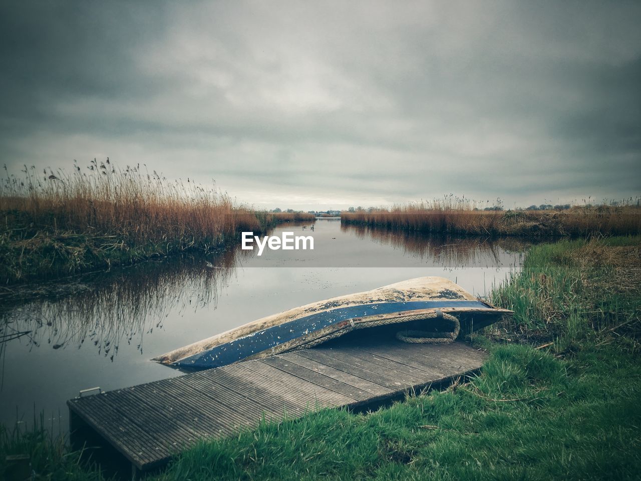 Old boat at jetty by river against cloudy sky