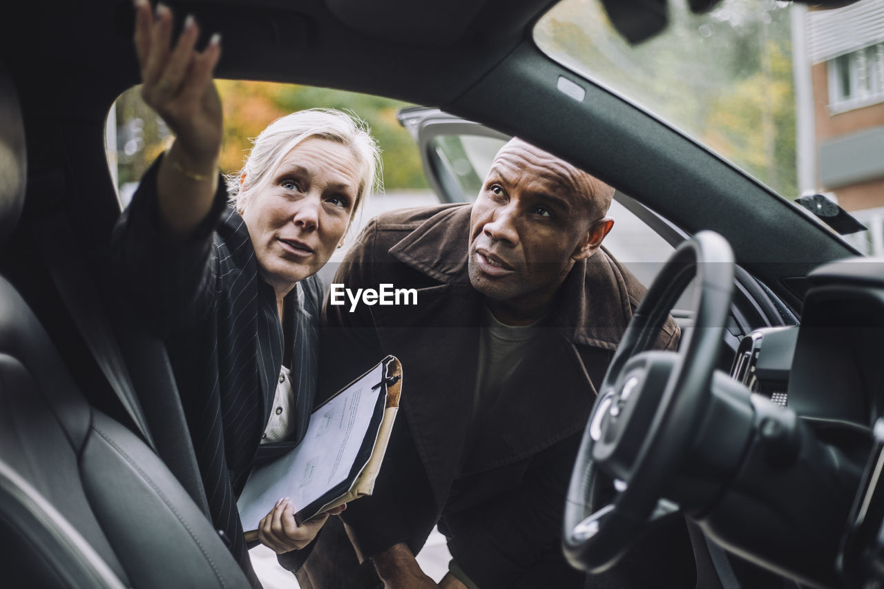 Saleswoman with documents explaining car features to male customer