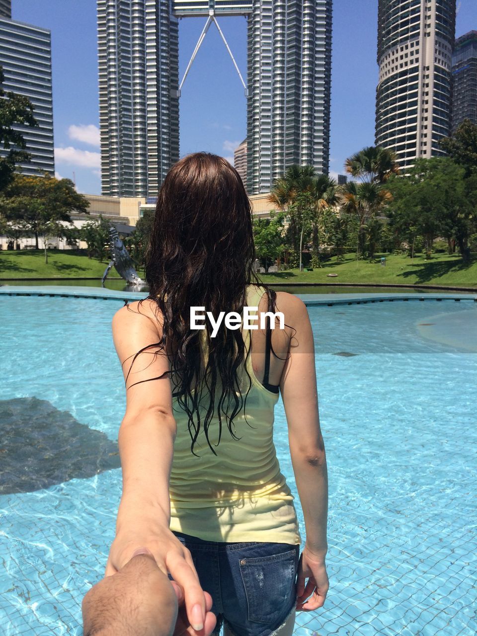 Rear view of woman holding hands while standing against swimming pool