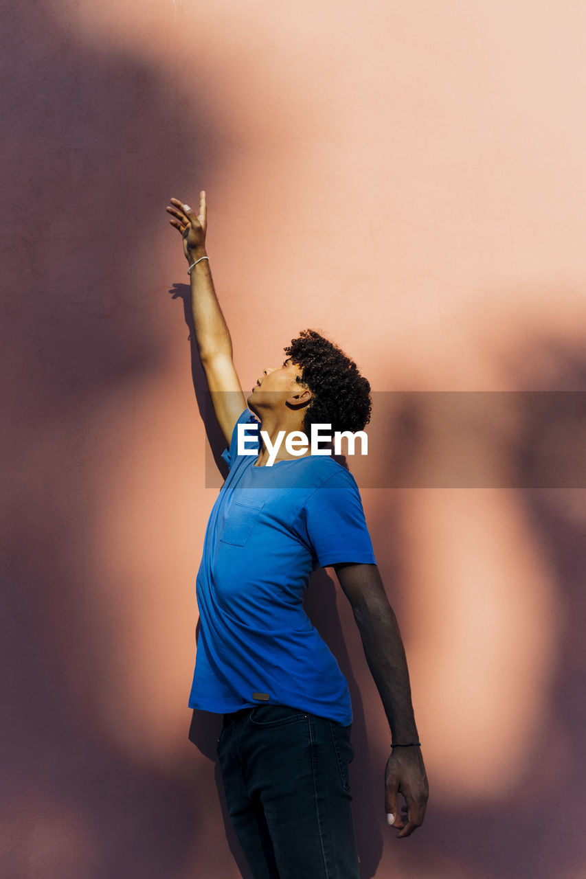 Young man with hand raised standing in front of wall