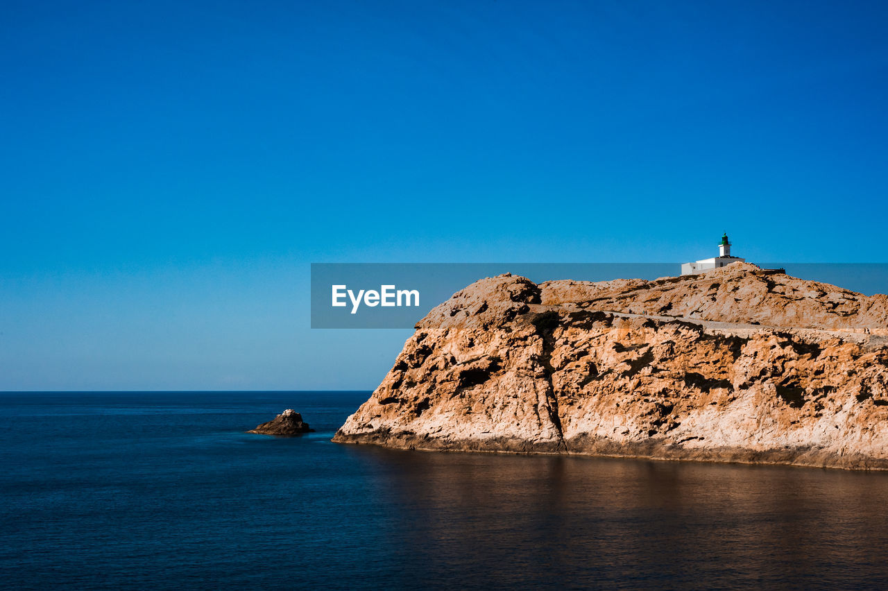 Rock formations by sea against clear blue sky