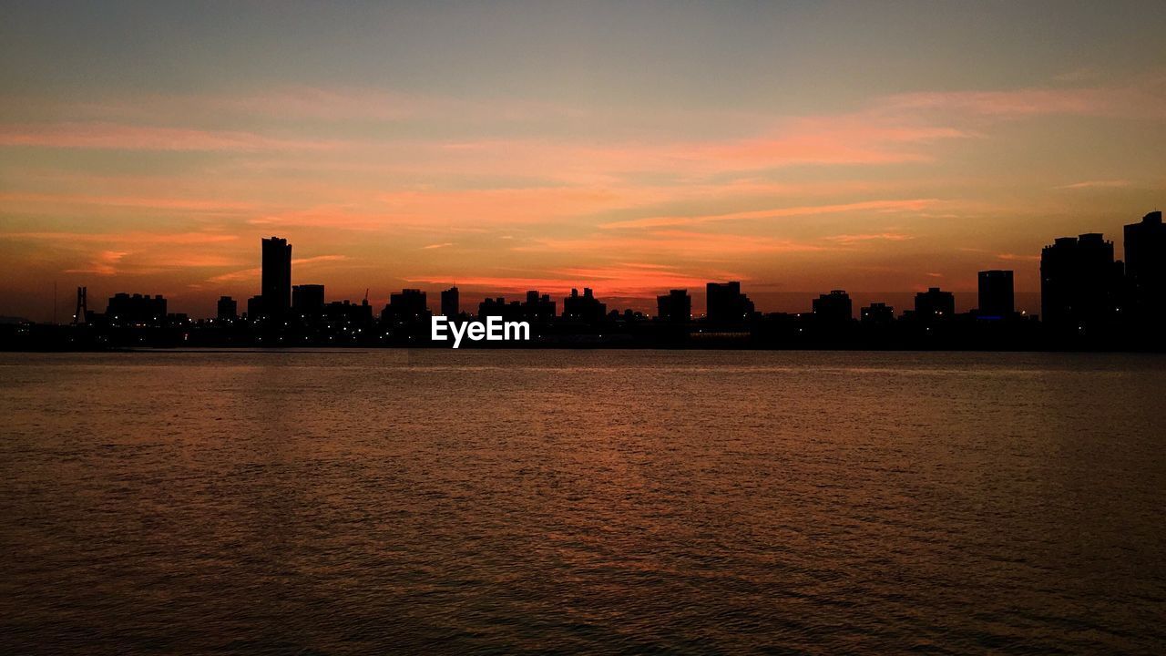 Scenic view of sea and urban skyline against sky during sunset