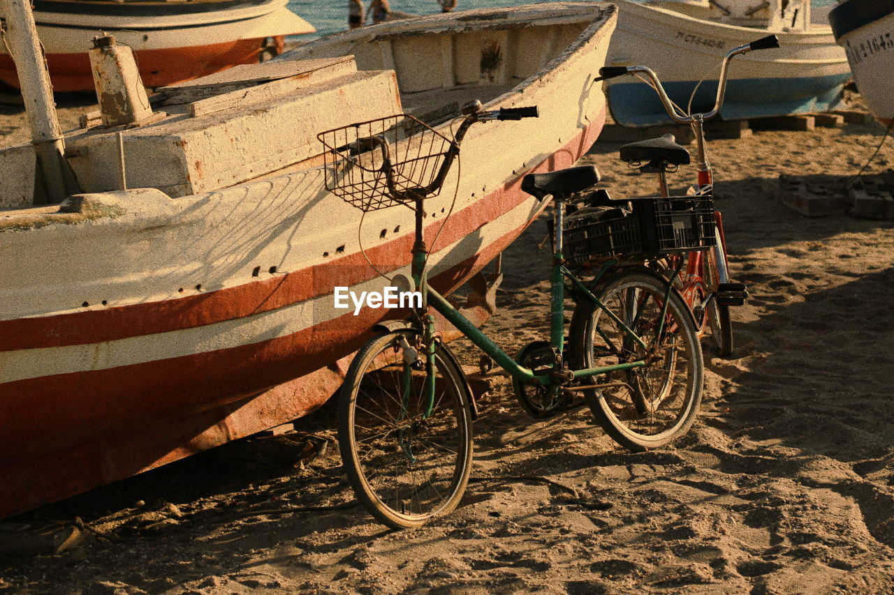 Bicycles parked by boat moored at beach during sunset