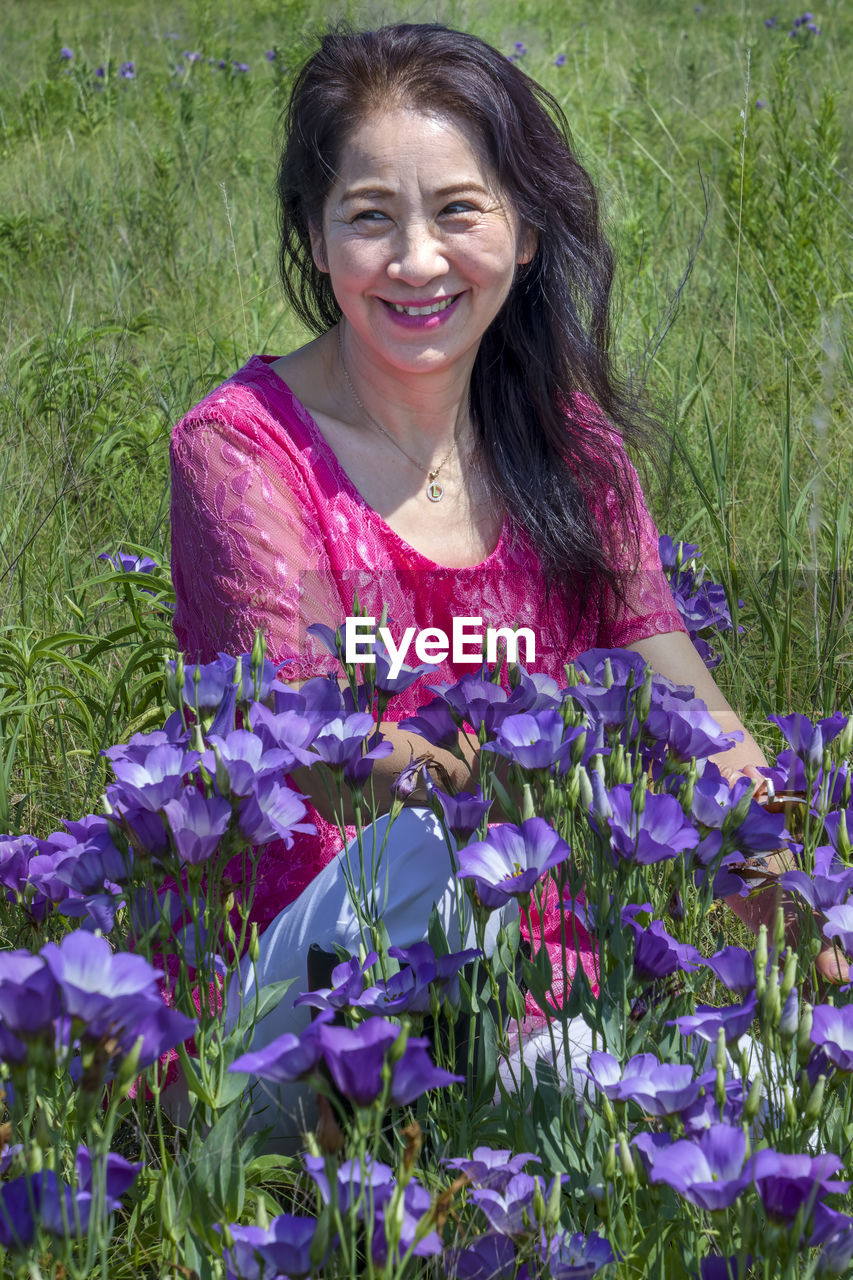 PORTRAIT OF A SMILING YOUNG WOMAN WITH PURPLE FLOWER IN FIELD