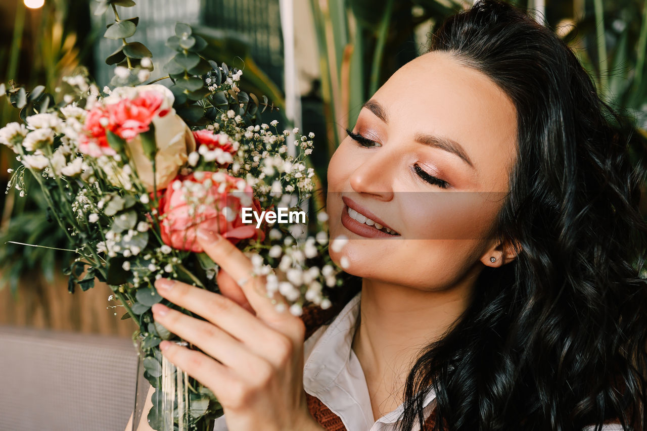 Portrait of a gentle attractive beautiful young brunette woman enjoying the smell of flowers